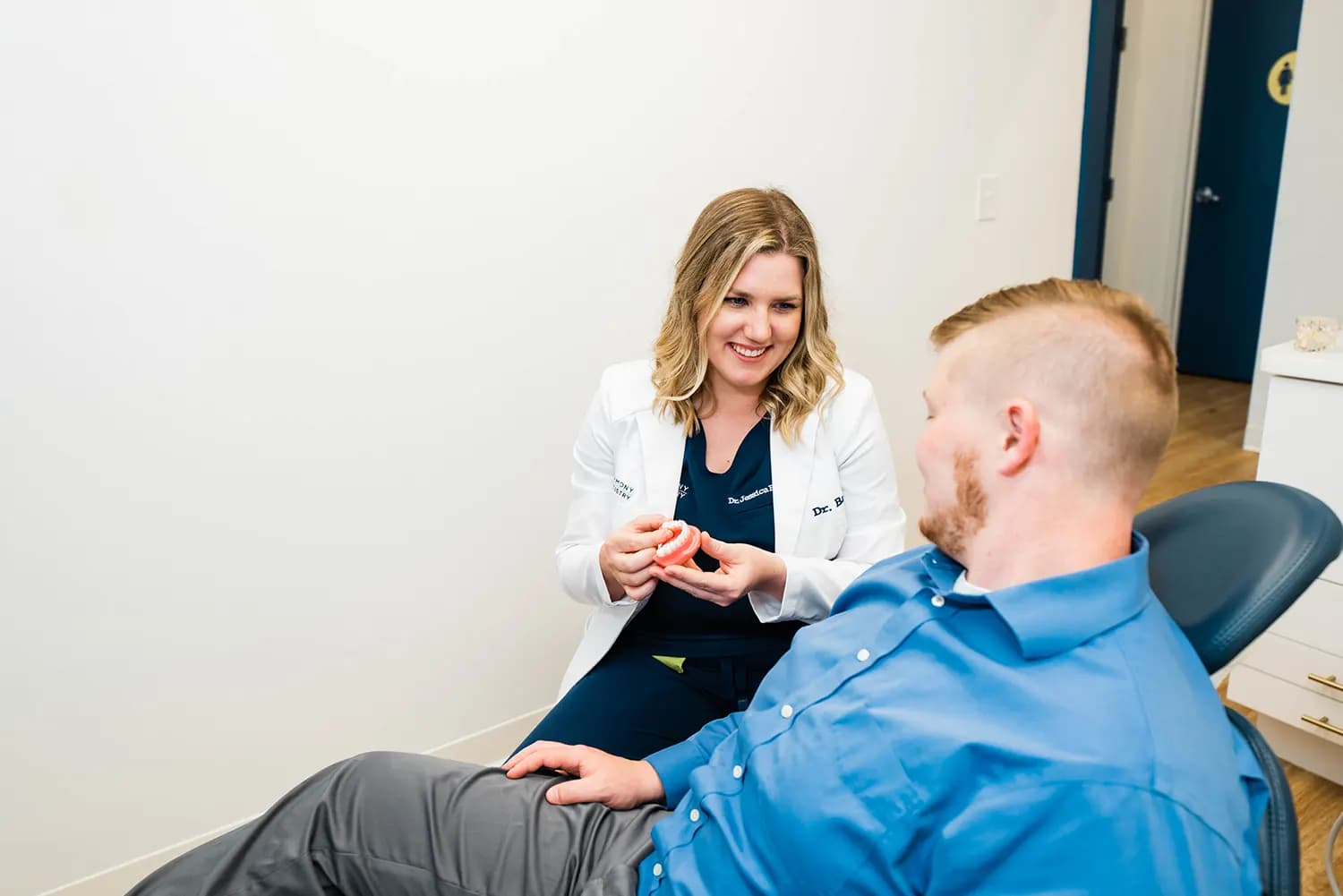 Smiling dentist in a white coat talks with a male patient seated in the dental chair