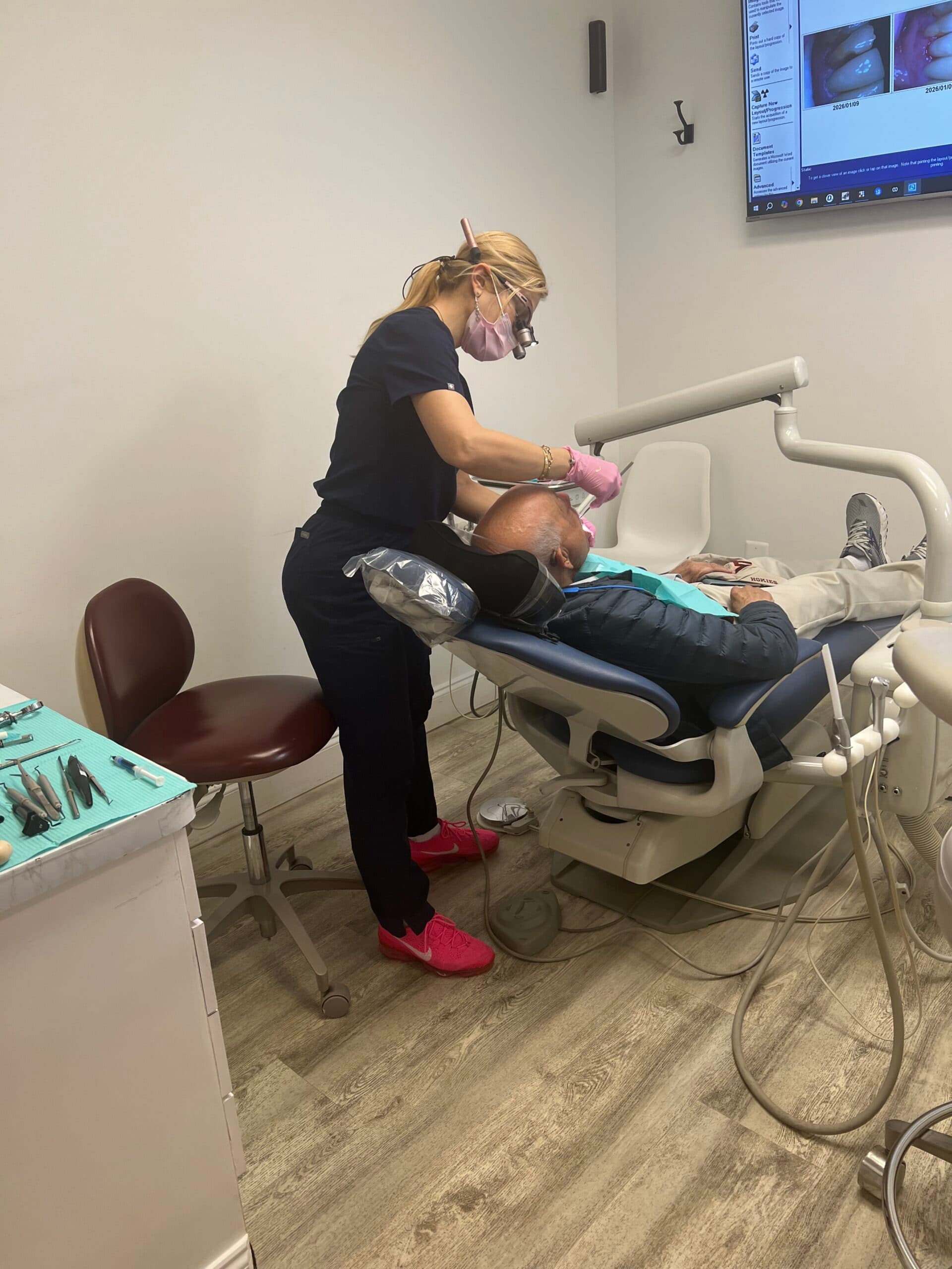 Alpine Dental team member in dark scrubs treating a reclined patient in a Burke, VA operatory