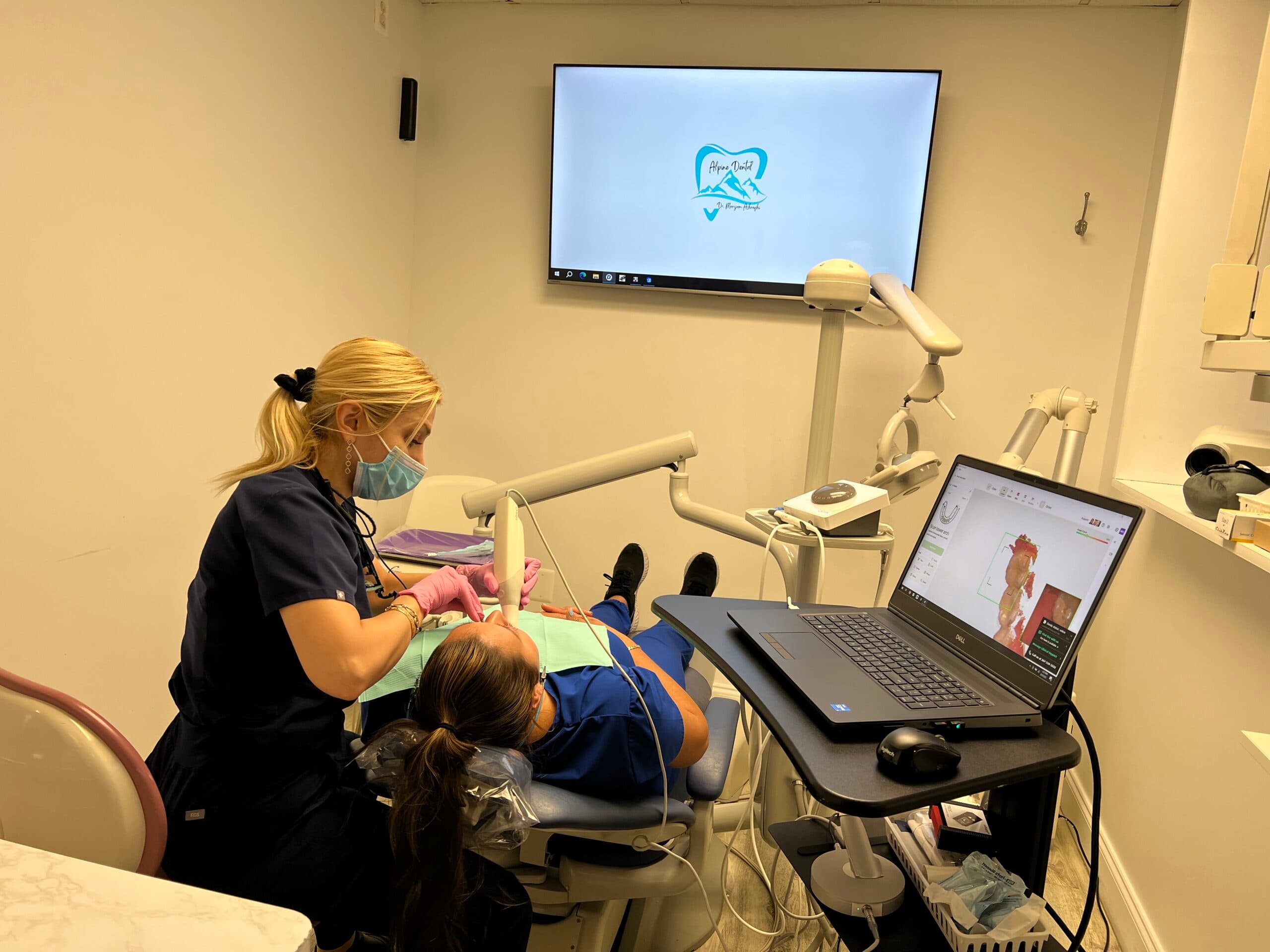 Alpine Dental hygienist examines a patient with a laptop and wall monitor in the Burke office