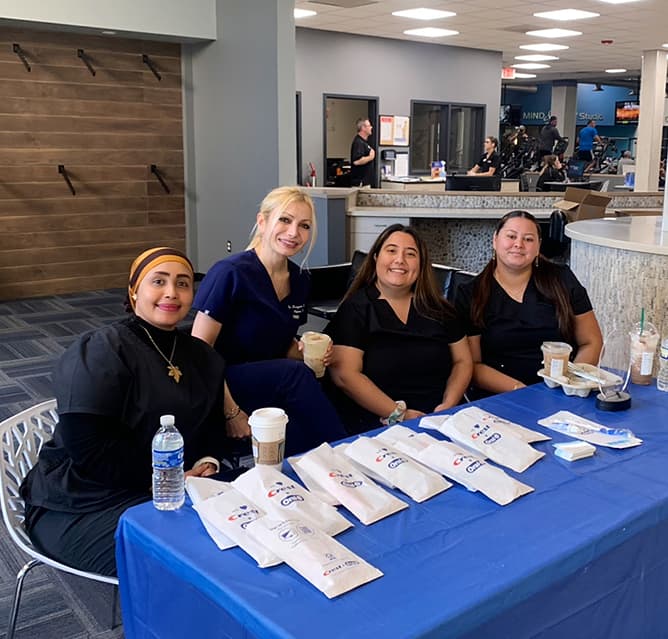 Four Alpine Dental team members seated at a community event table with dental care kits