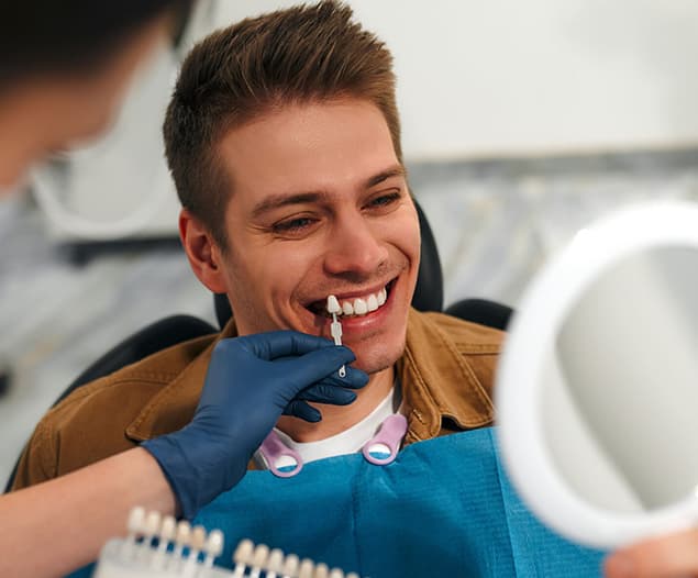 Smiling man in the dental chair as a veneer shade guide is held to his teeth