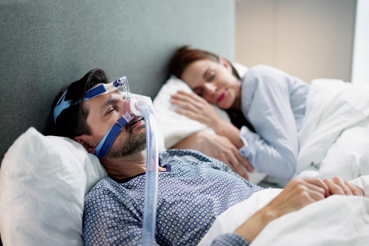 Man using a CPAP machine for sleep apnea treatment while sleeping at home in Burke, VA